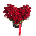 Heart-shaped arrangement of red roses in a black box with a red ribbon on a white background