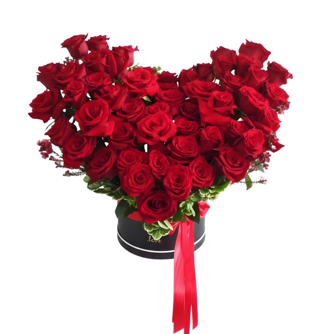 Heart-shaped arrangement of red roses in a black box with a red ribbon on a white background