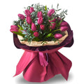 Bouquet of pink tulips with greenery wrapped in pink paper and ribbon on a white background