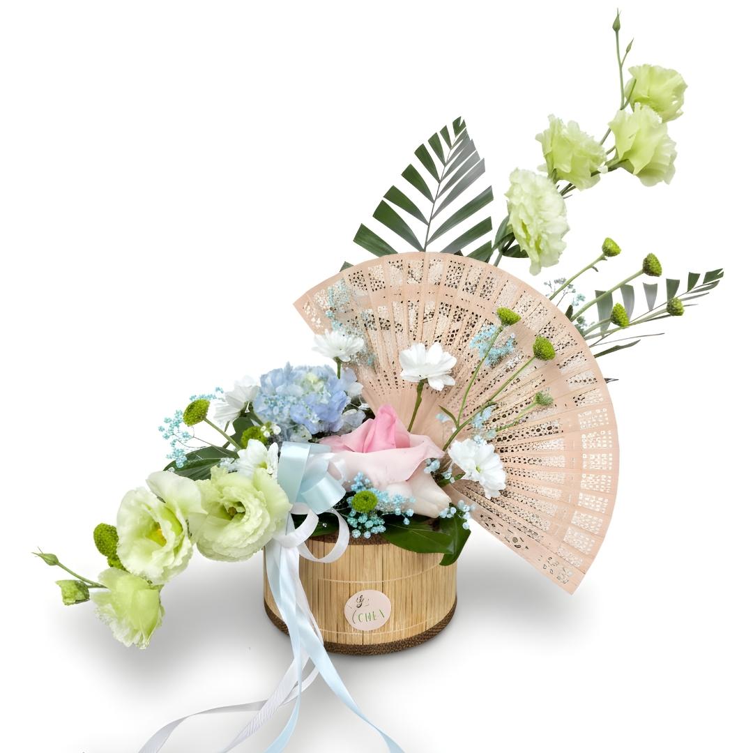 Floral arrangement with a fan and ribbons in a wooden box on a white background