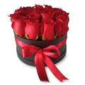 Round black box filled with red roses and a red ribbon on a white background